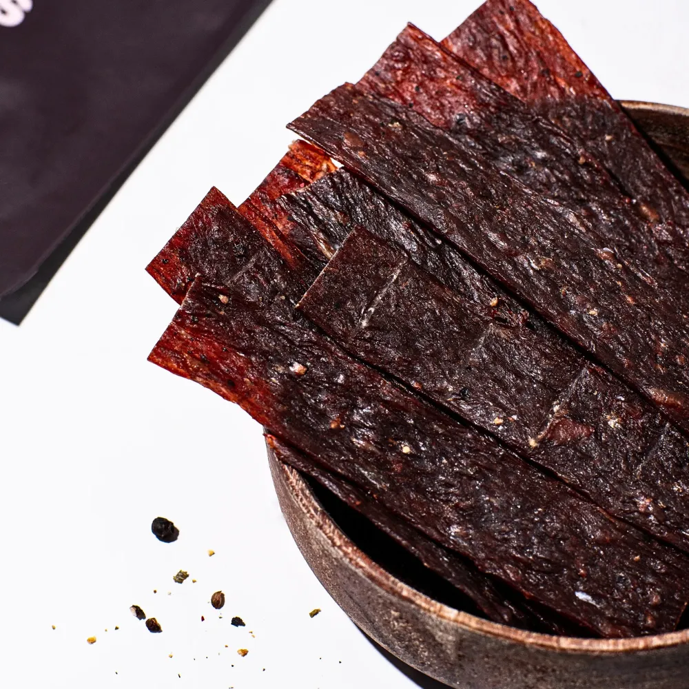 Suszone plastry wołowiny BIO z czarnym pieprzem - zbliżenie struktury mięsa.